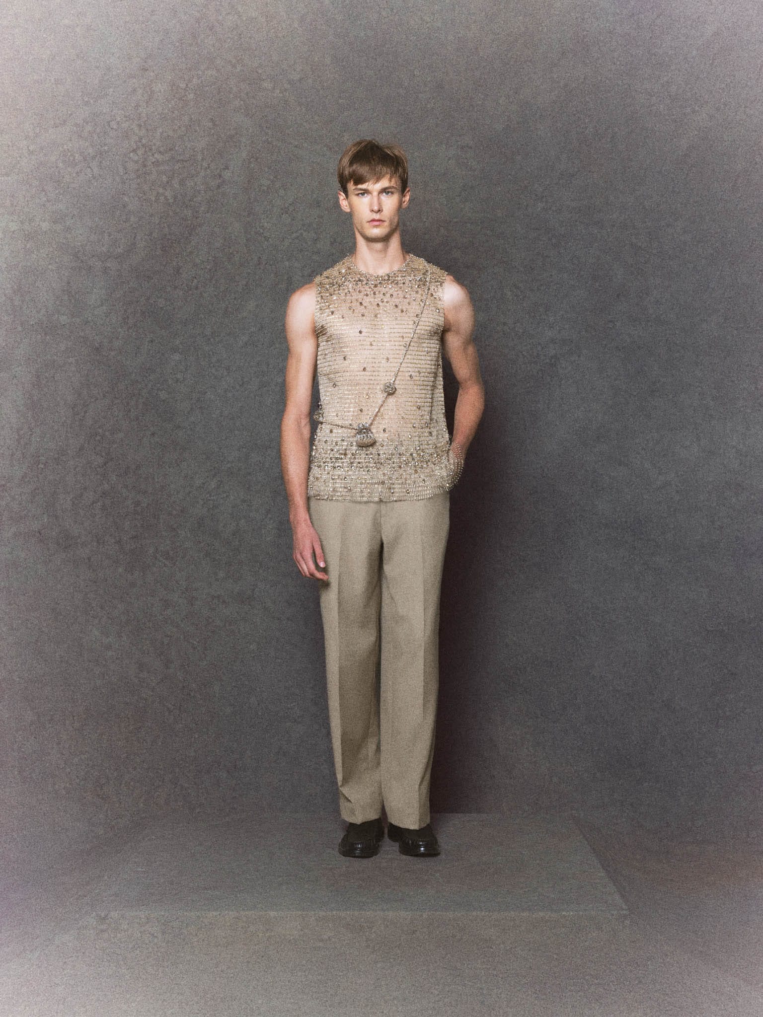 Nude mesh sleeveless top with crystal embellishments paired with gray trousers